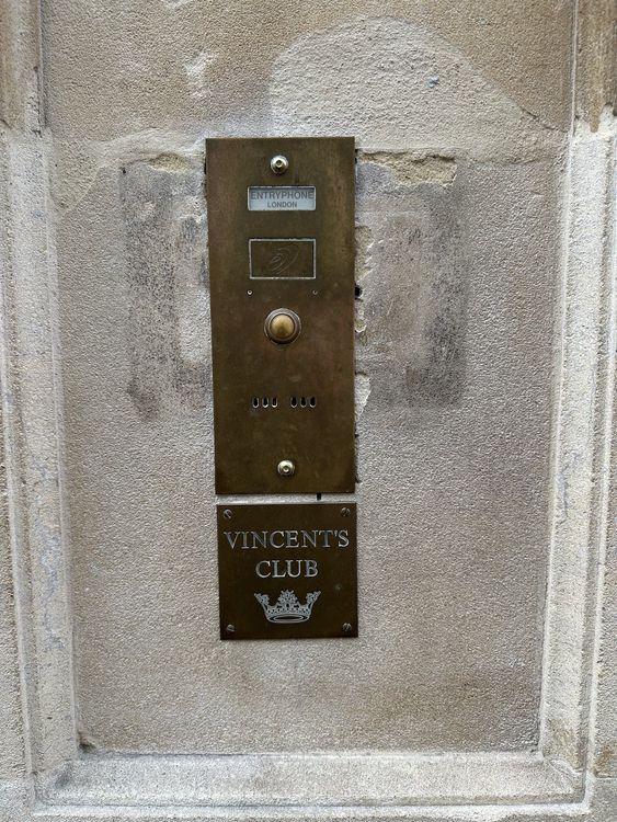 The brass entryphone beside the door of Vincent's Club, with the club's name and crown on the plate below the bell.